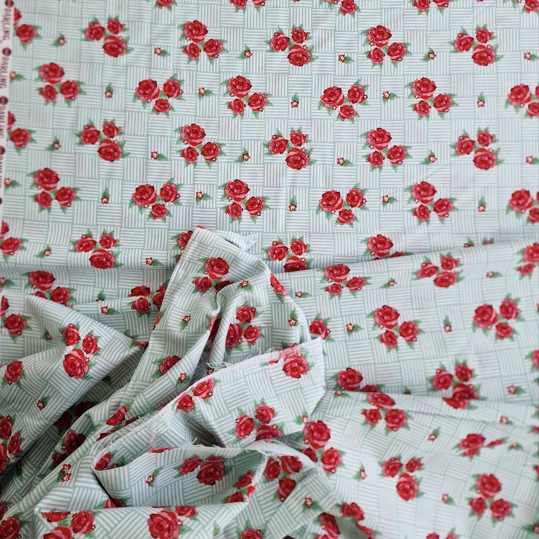 A piece of cotton fabric with a floral pattern, predominantly red roses on a green and white background, folded loosely. available at Eau Brink Studio