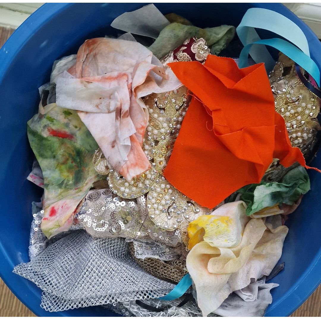 Open scrap bin in textile artist's studio filled with loosely thrown colorful fabric remnants, ready for creative use.