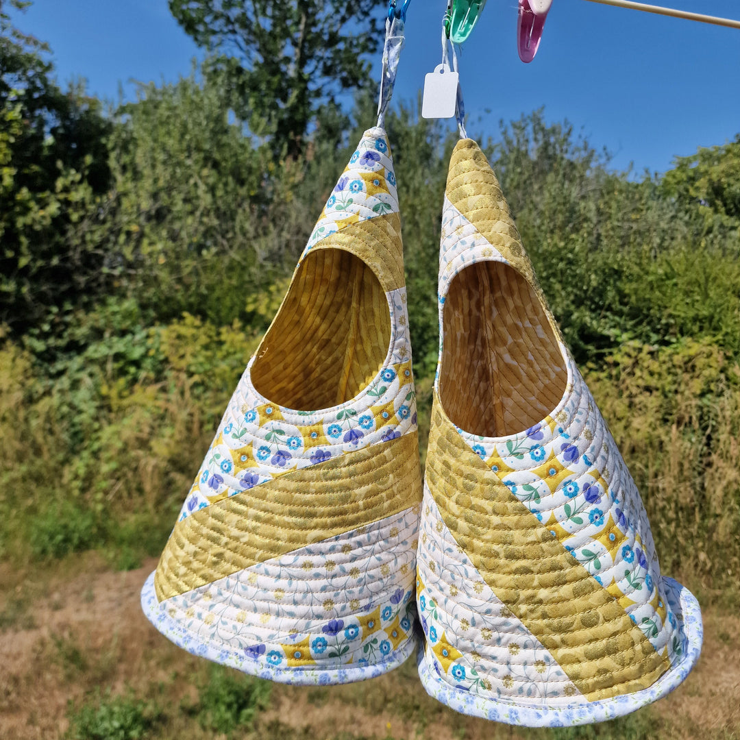 Two hanging baskets with blue and yellow floral patterns, suspended outdoors on a clothesline against a background of trees and sky.