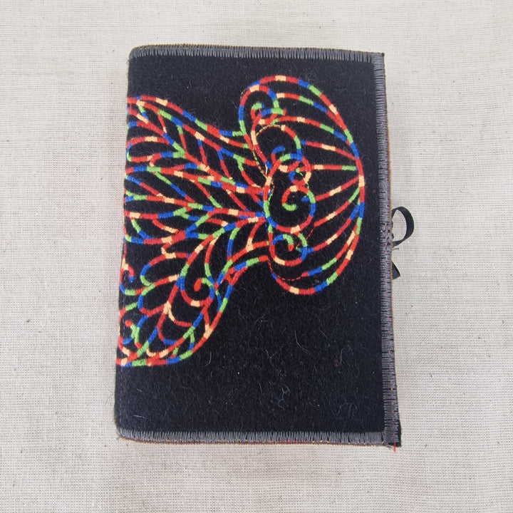 A small black fabric Needlecase cover with a colourful embroidered jellyfish design, shown on a light beige textured fabric background.