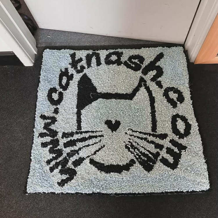 Doormat with cat design and 'www.catnash.com' text on a carpeted floor.