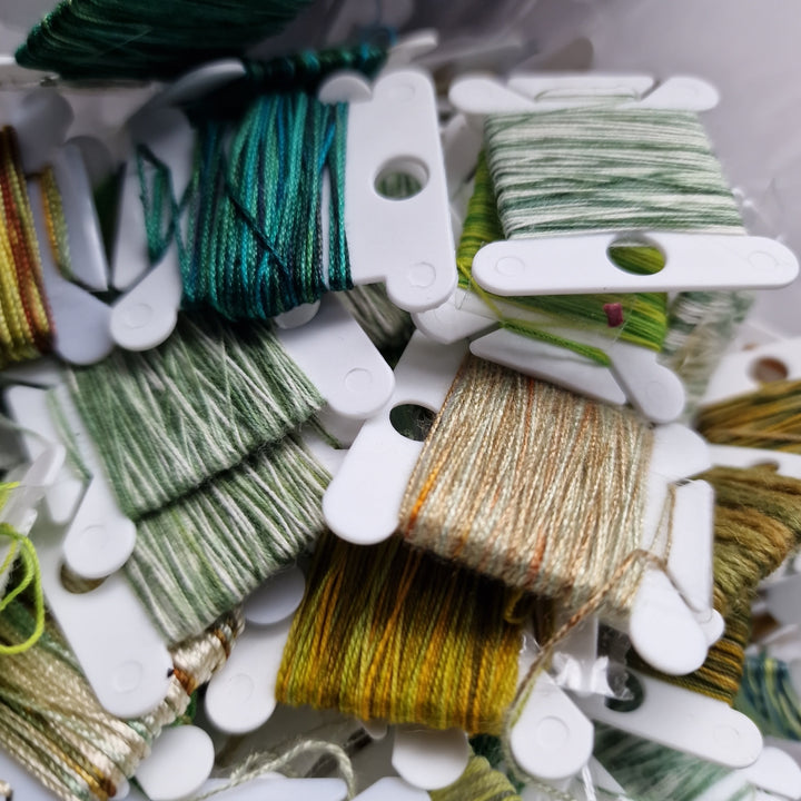 Collection of green and gold embroidery threads on white bobbins.